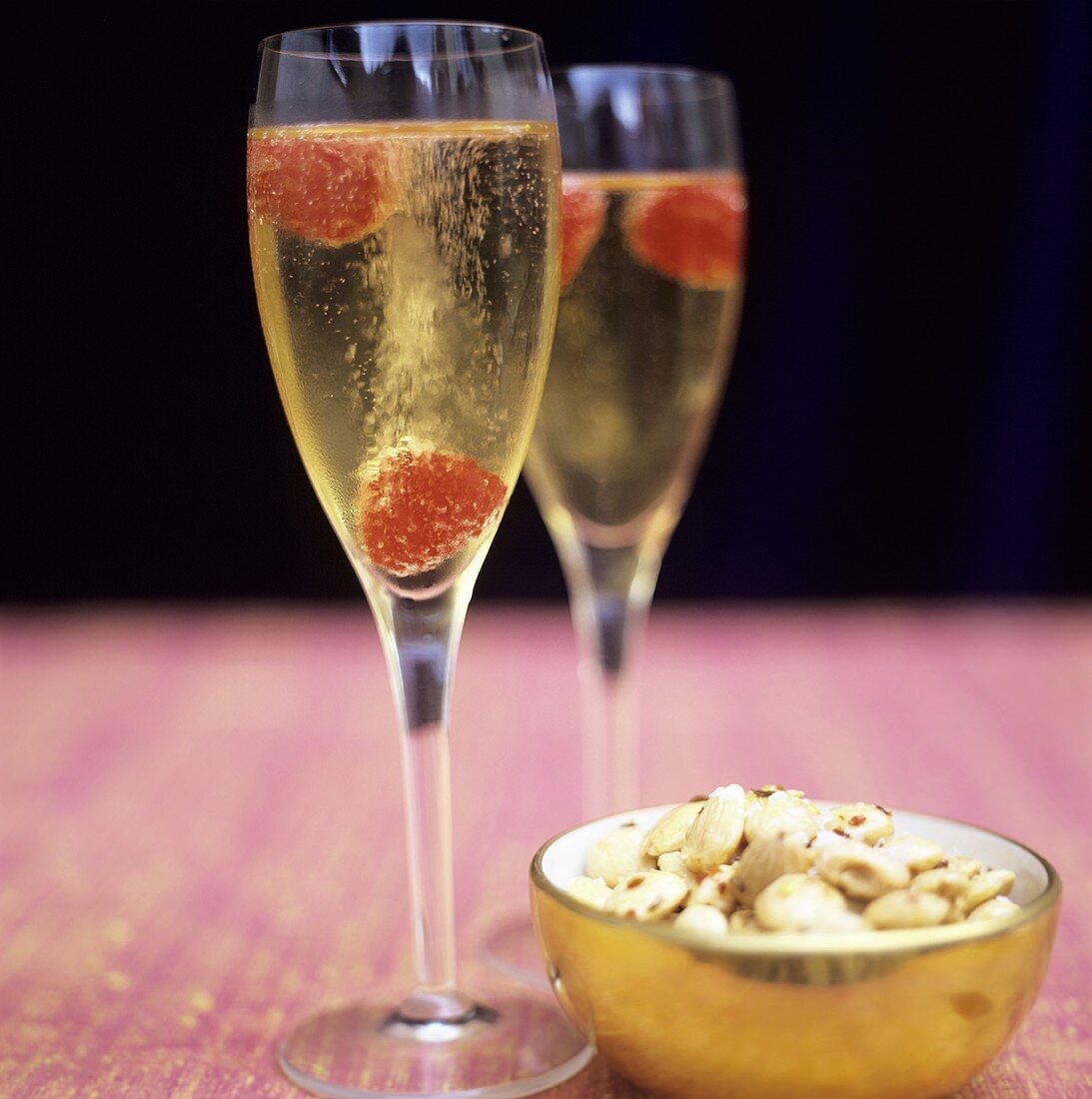 Two glasses of champagne with raspberries & bowl of almonds