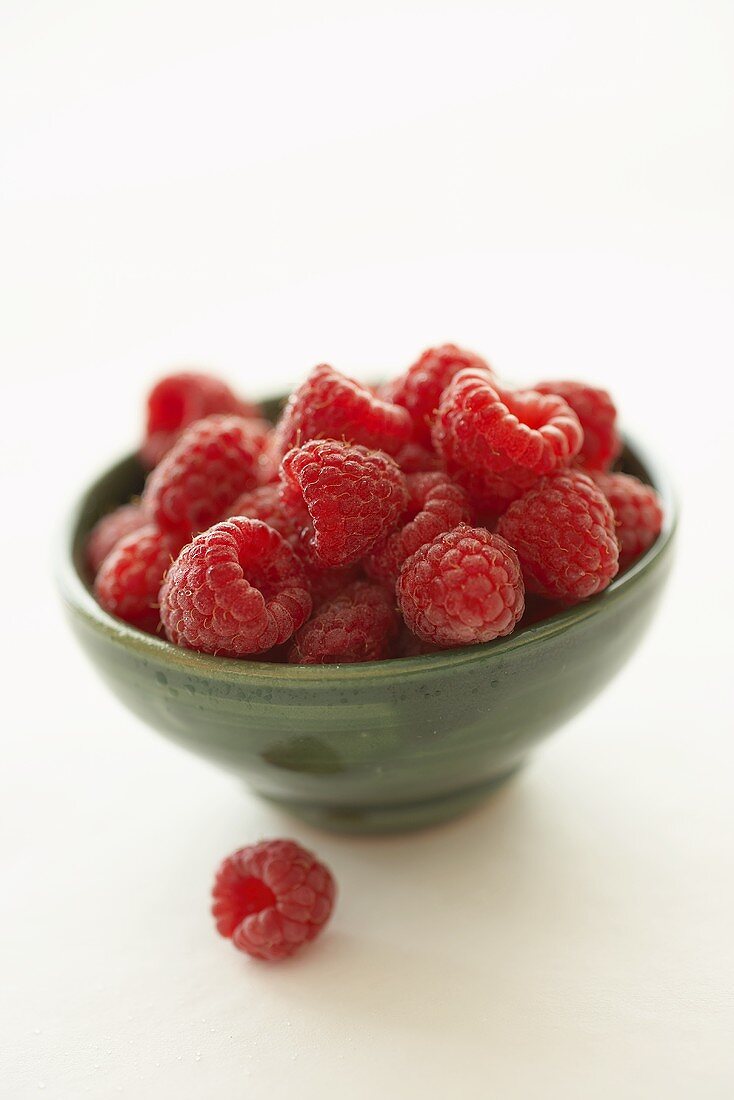 Small bowl of raspberries, one raspberry in front