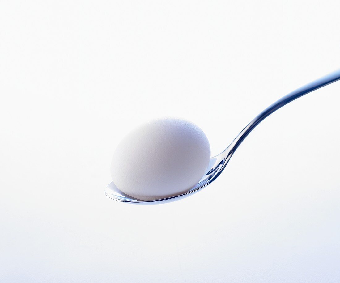 Ein weisses Ei auf einem Löffel vor weißem Hintergrund