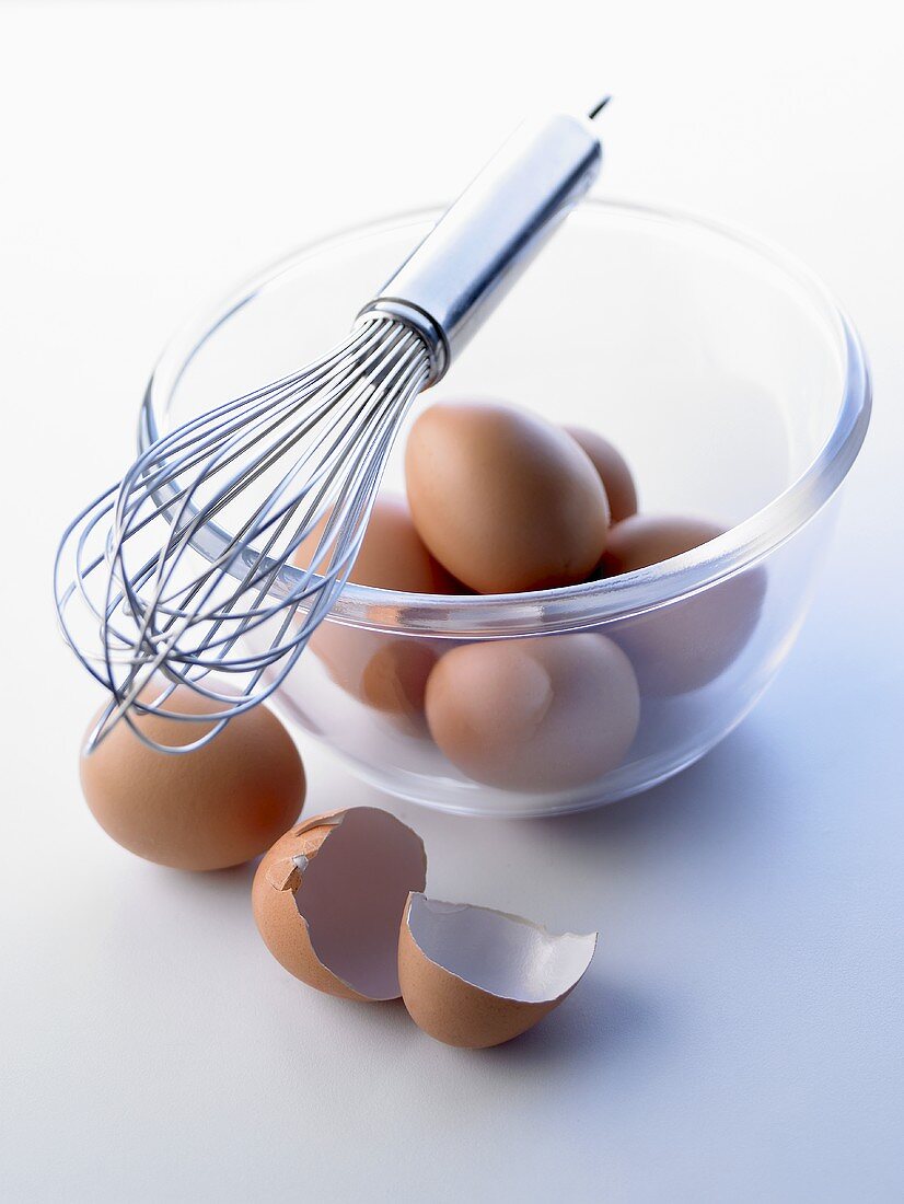 Brown eggs in a glass bowl, egg whisk on bowl