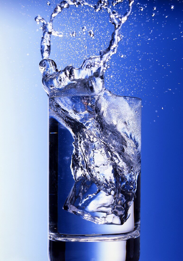 Eiswürfel fällt in Wasserglas