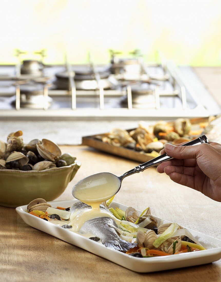 Pouring sauce over sea bass and mussels