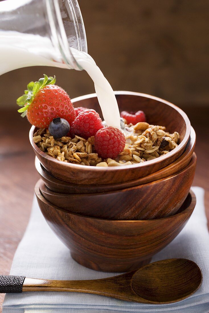 Milch zu Müsli und Beeren in Müslischale gießen