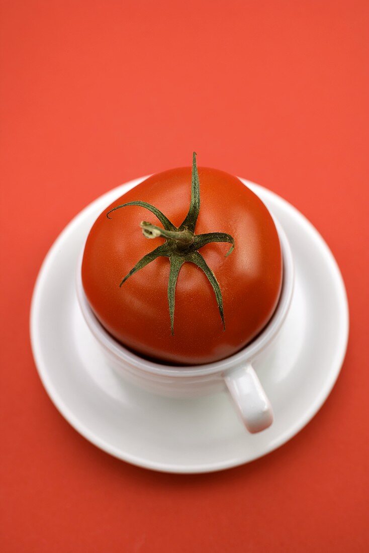 Red tomato in coffee cup against red background