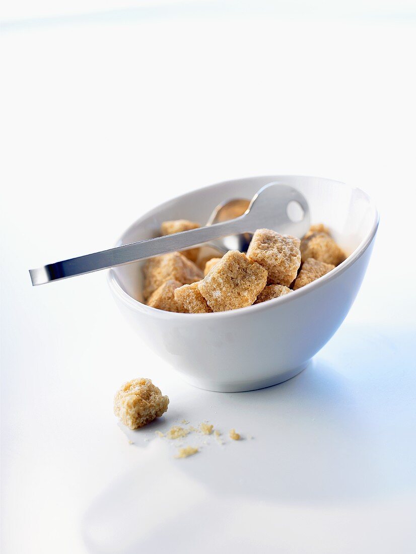 Brown sugar cubes in a small bowls with sugar tongs