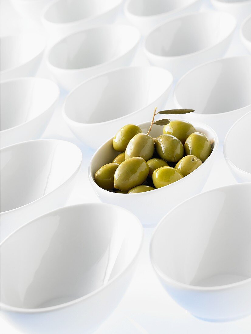 Viele weiße Schalen, eine davon mit grünen Oliven gefüllt