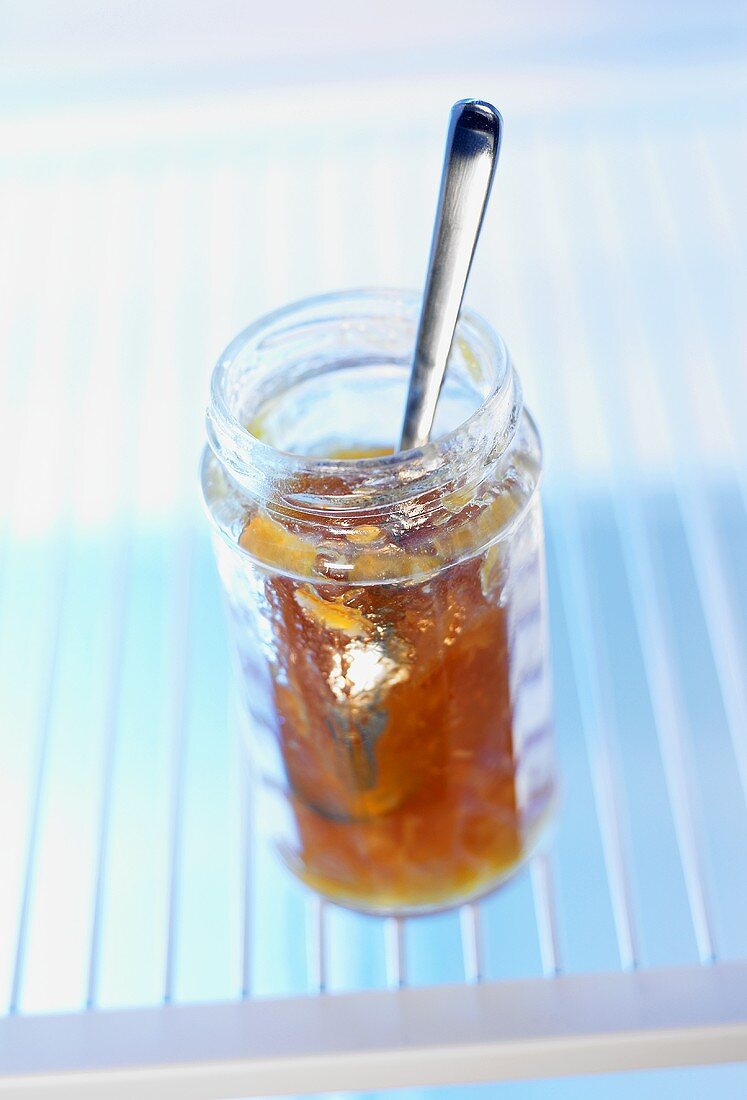 Opened jam jar with spoon in fridge