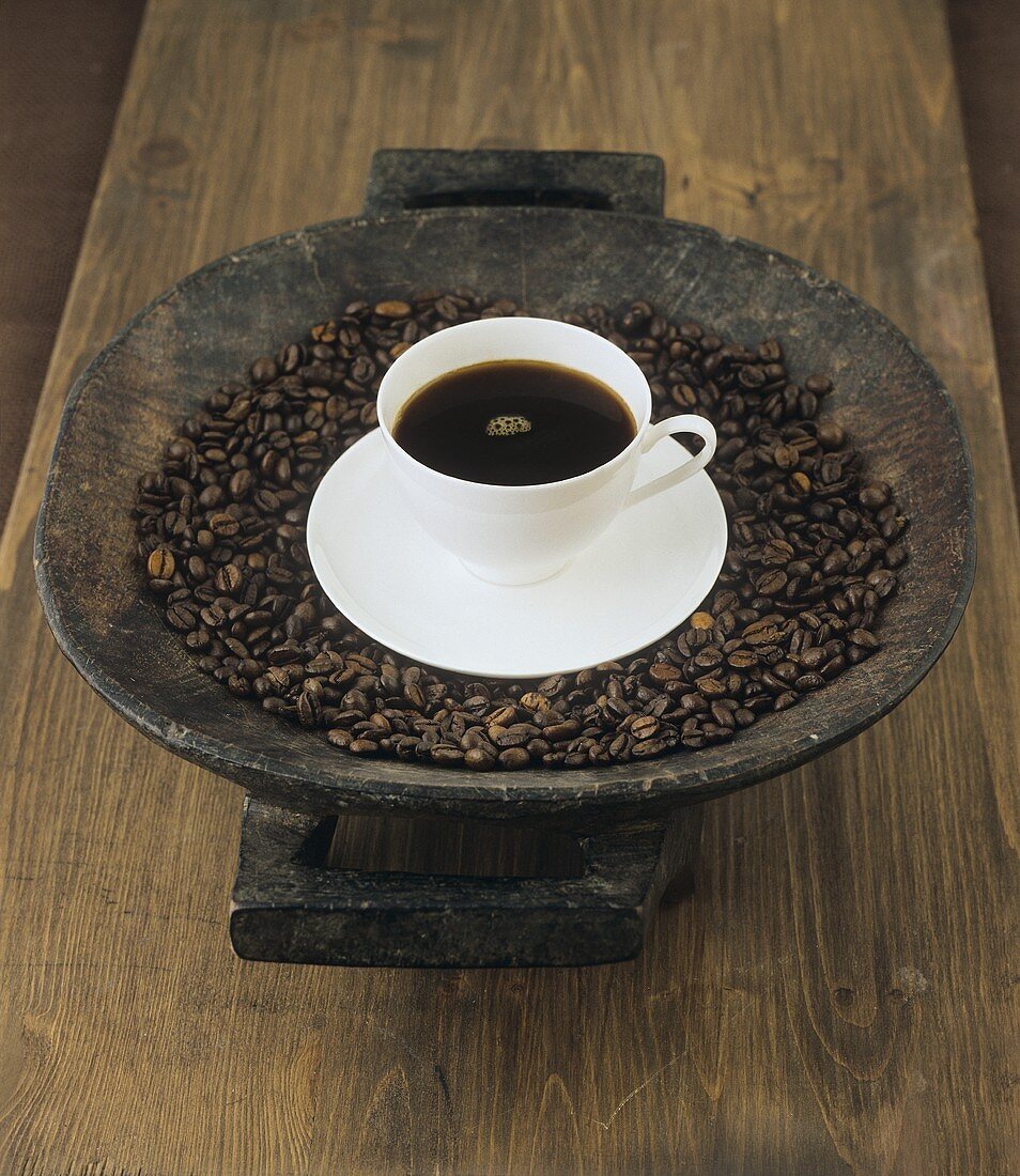 A cup of coffee on coffee beans in a wooden bowl