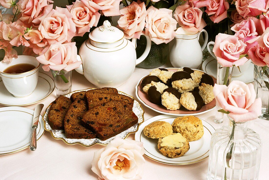 Fruit loaf, scones, cookies and tea on table with roses