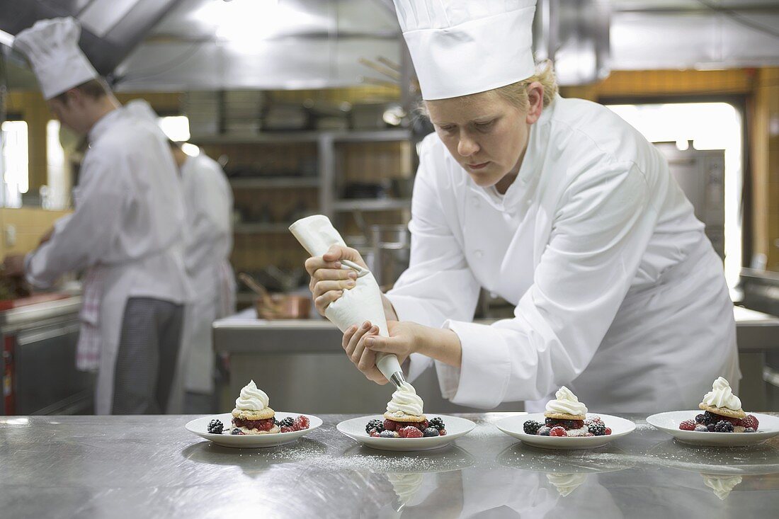 Female chef piping cream onto desserts