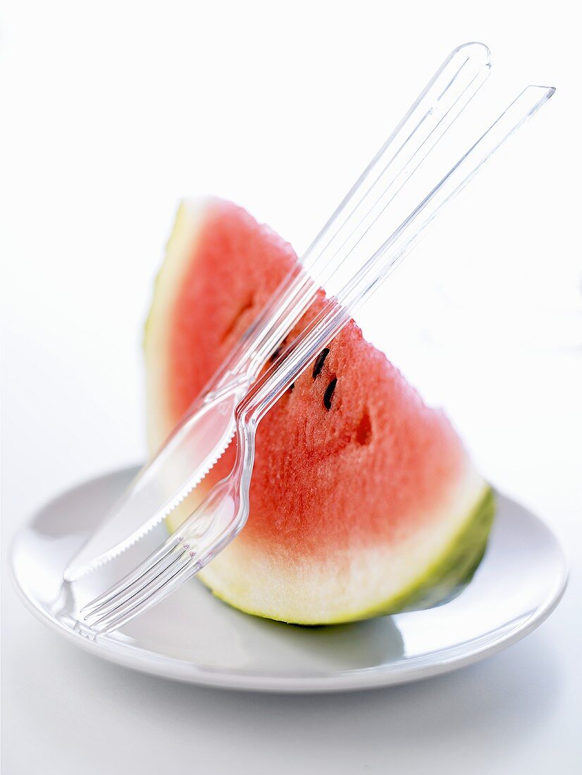 A piece of watermelon on a plate with plastic cutlery