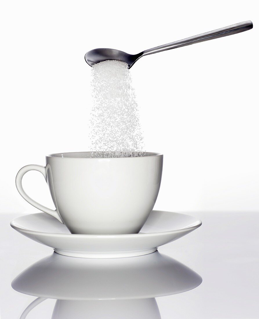 Zucker rieselt vom Löffel in eine Tasse