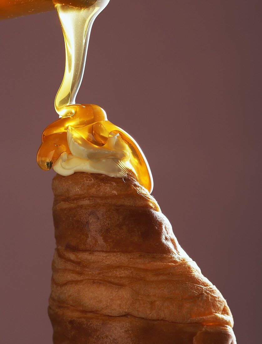 Honig fließt auf ein Croissant mit Butter