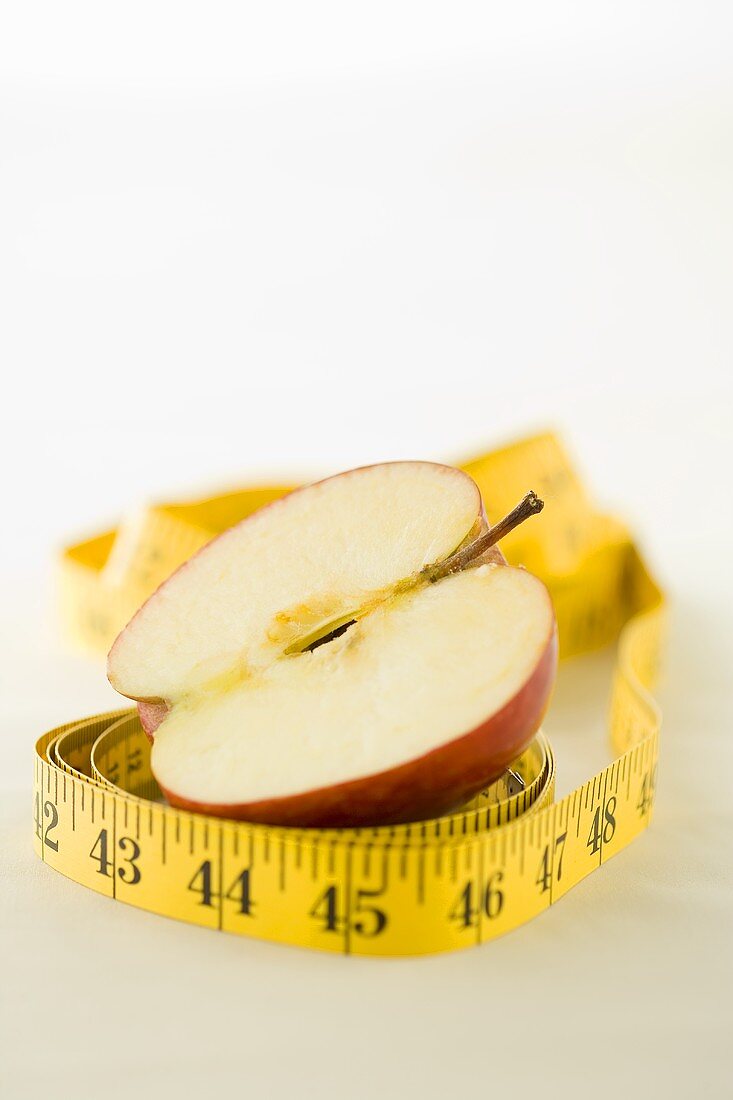 Ein Massband liegt um einen halben Apfel