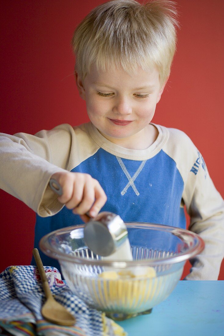 Small boy tipping sugar into a bowl