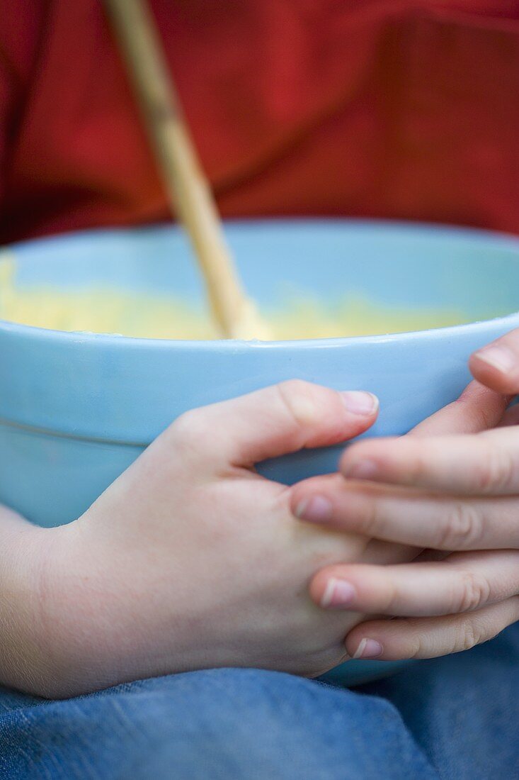 Child's hands holding a bowl of cake mixture