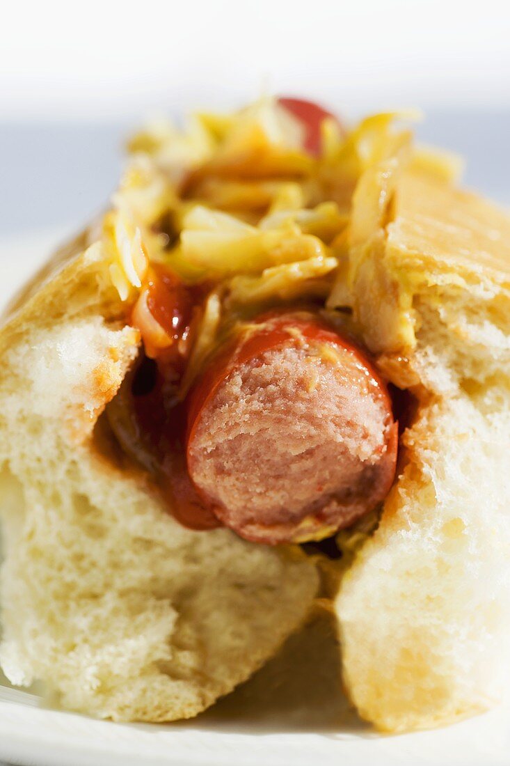Ein angebissener Hot Dog mit Zwiebeln, Ketchup, Senf und Käse