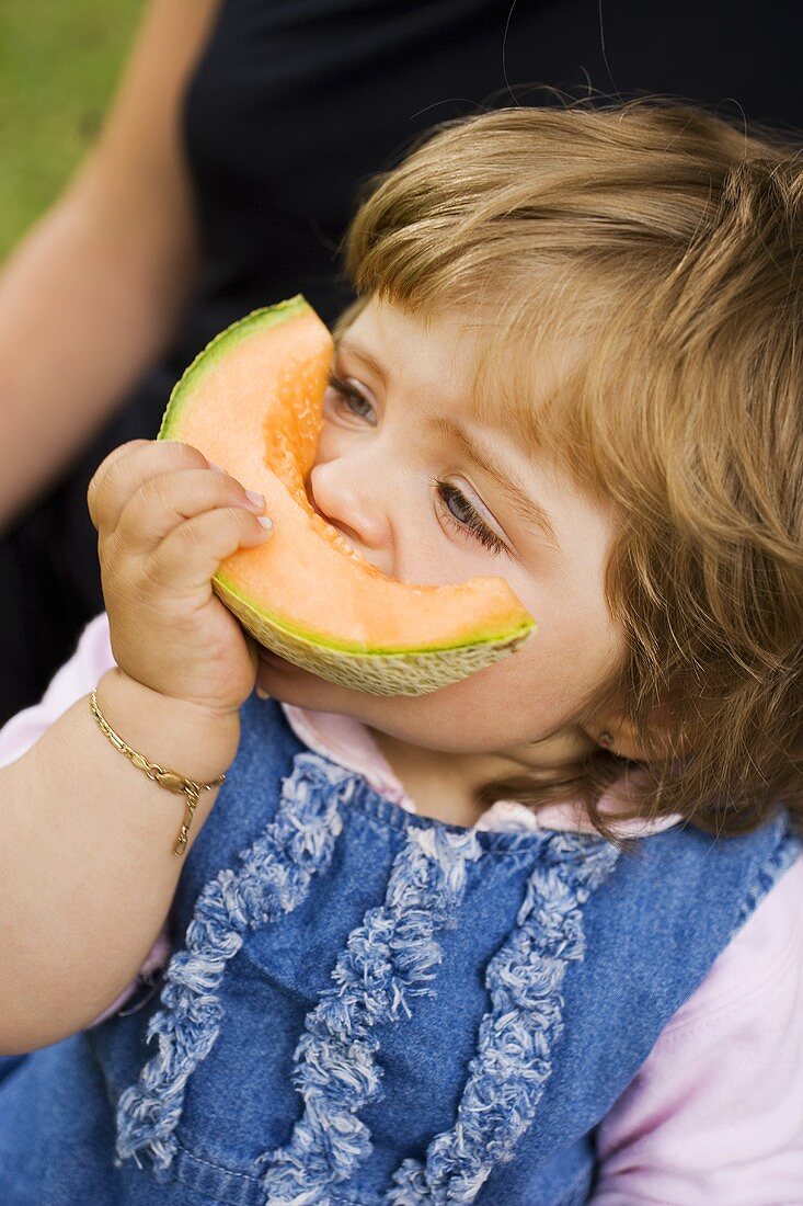 Kleines Mädchen beisst in eine Honigmelonen-Spalte