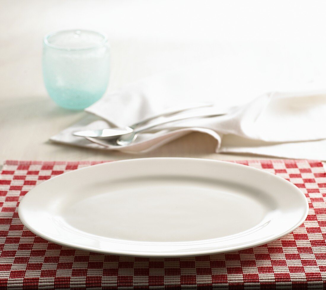 A place-setting with table-mat, plate, cutlery and napkin