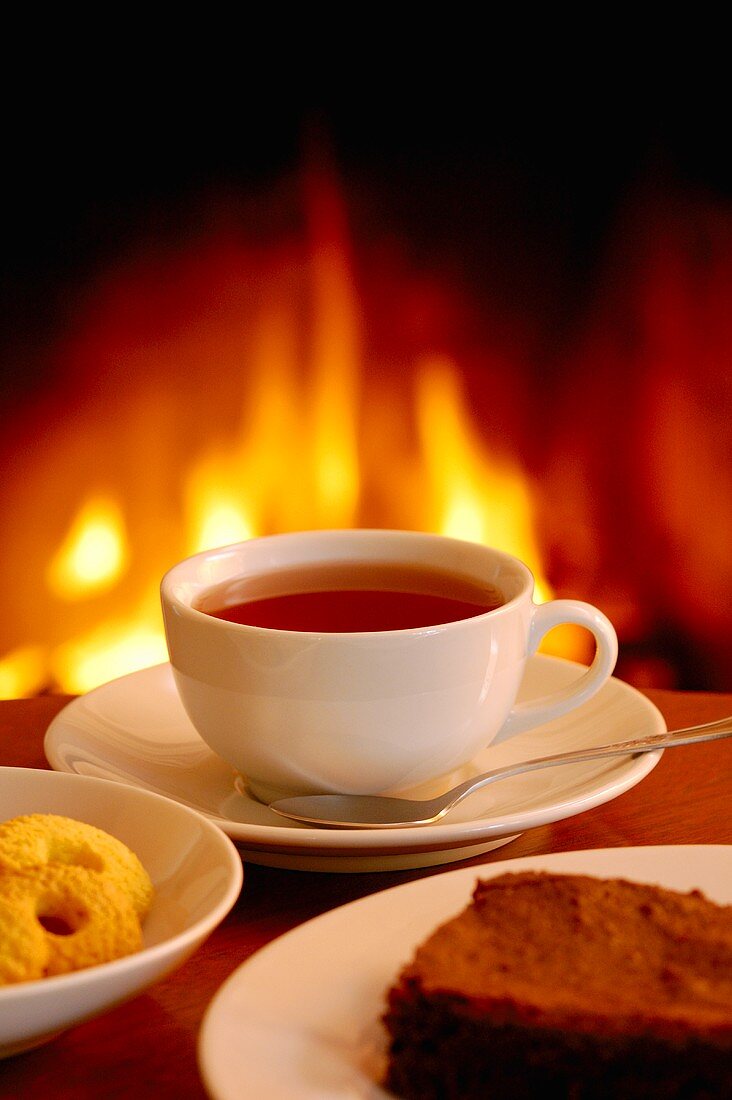 A cup of coffee with cake and biscuits by the fireside
