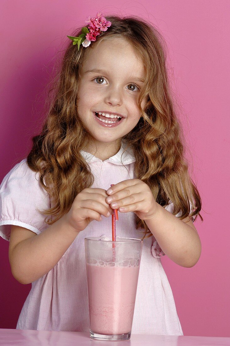 Kleines Mädchen steht hinter einem Glas Erdbeermilch