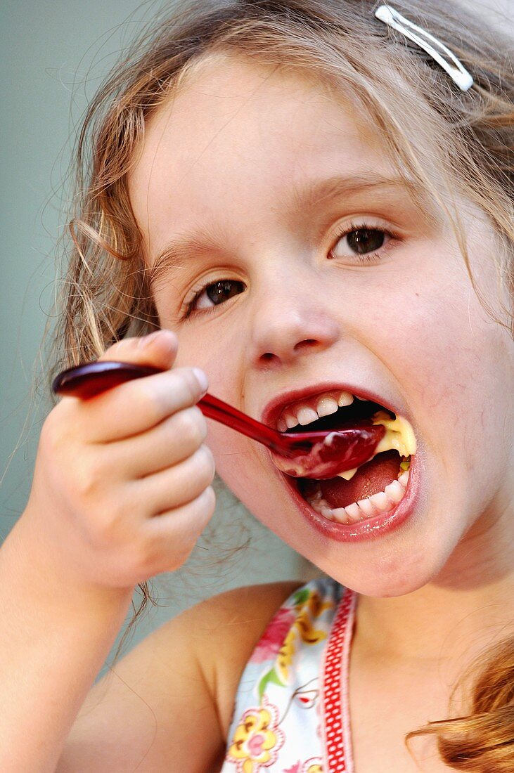 Kleines Mädchen isst Vanillepudding mit einem Plastiklöffel