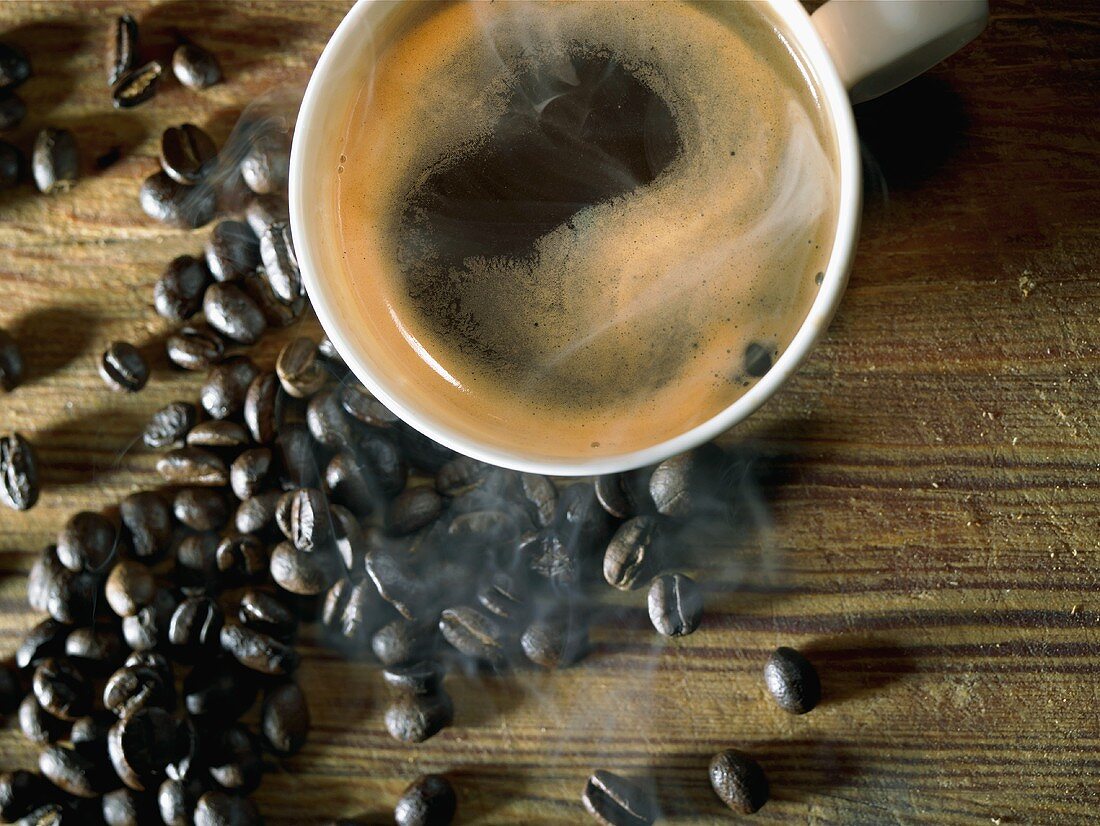 A cup of coffee surrounded by coffee beans