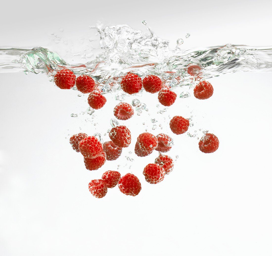 Fresh raspberries falling into water