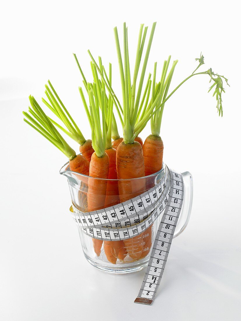 Fresh carrots in measuring jug with tape measure