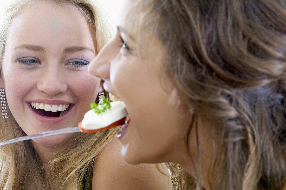 Two young women eating tomato with mozzarella