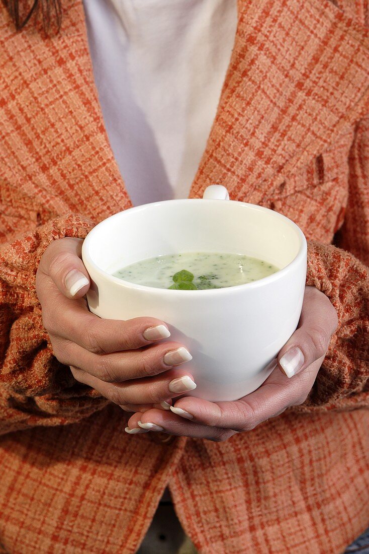 Two hands holding a cup of broccoli cream soup