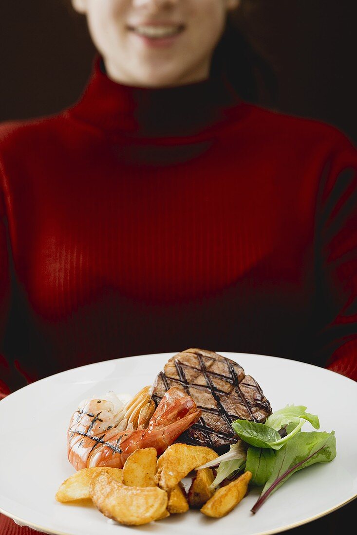 Frau hält Teller mit Surf and Turf (Rindersteak mit Garnele)