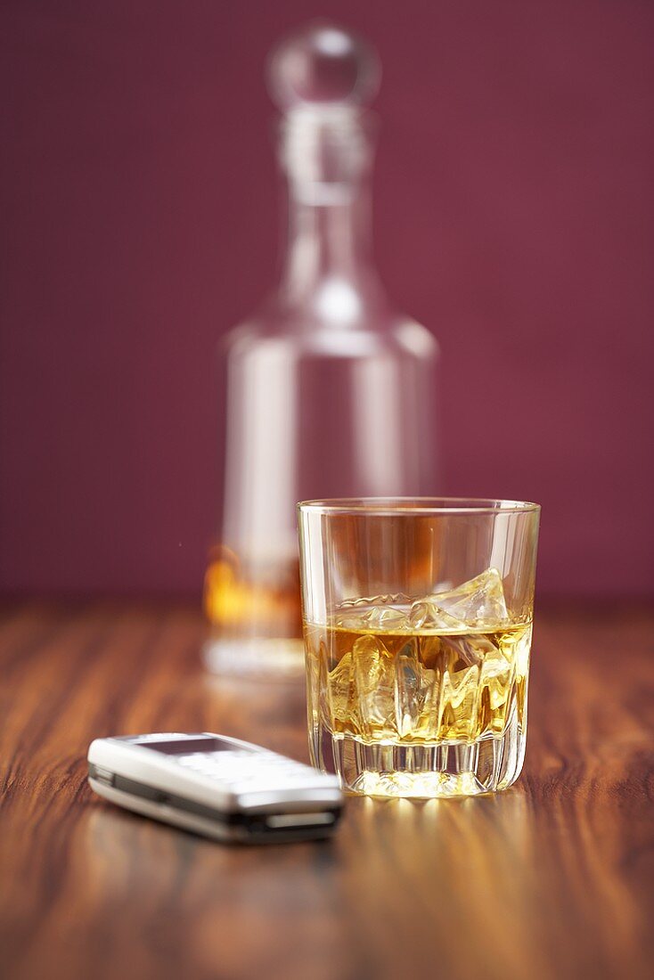 Whiskey in Glas und Karaffe, daneben Handy