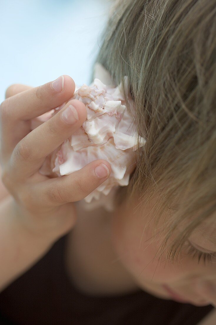 Kind hält Muschelschale ans Ohr