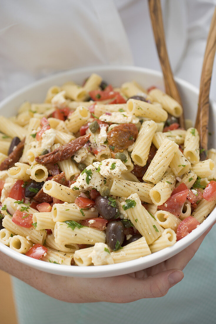 Frau hält Schüssel Nudelsalat mit Tomaten und Oliven