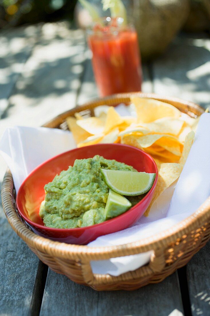 Guacamole with tortilla chips in a basket, tomato drink