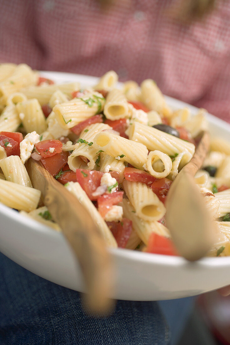 Person hält Schüssel Nudelsalat mit Tomaten und Oliven