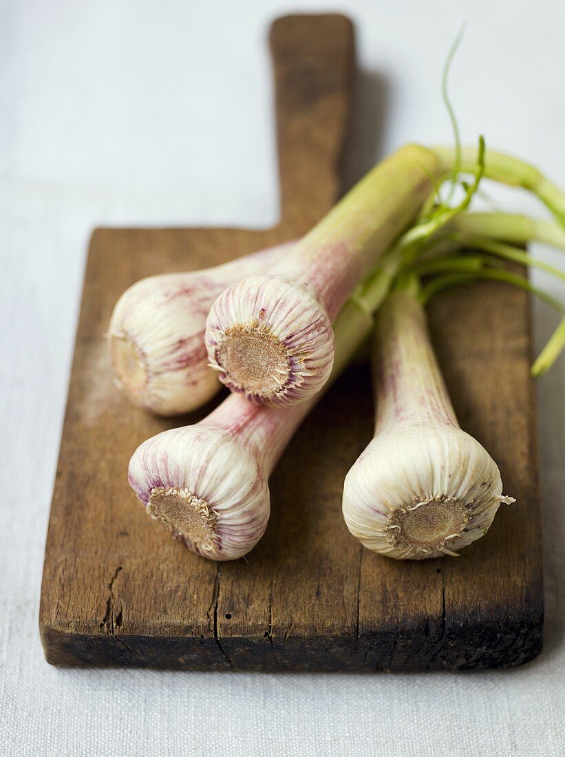 Four garlic bulbs on rustic chopping board