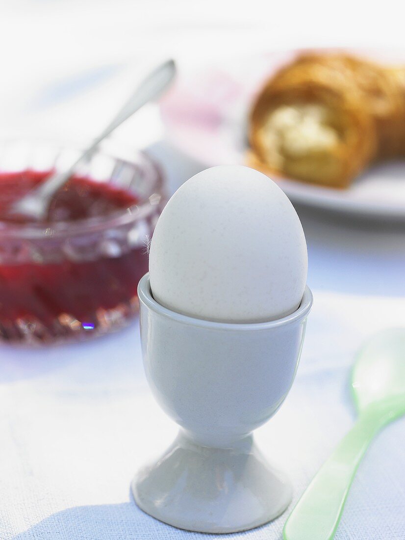 Boiled egg in an eggcup, jam and croissant