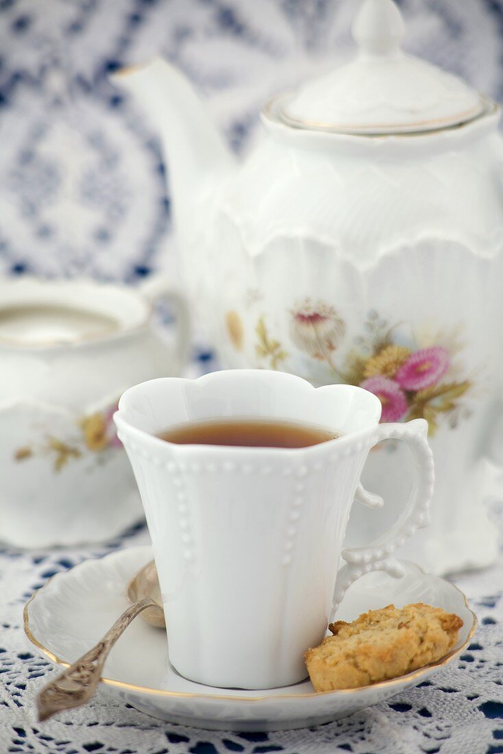 A cup of black tea with teapot, sugar bowl and biscuit