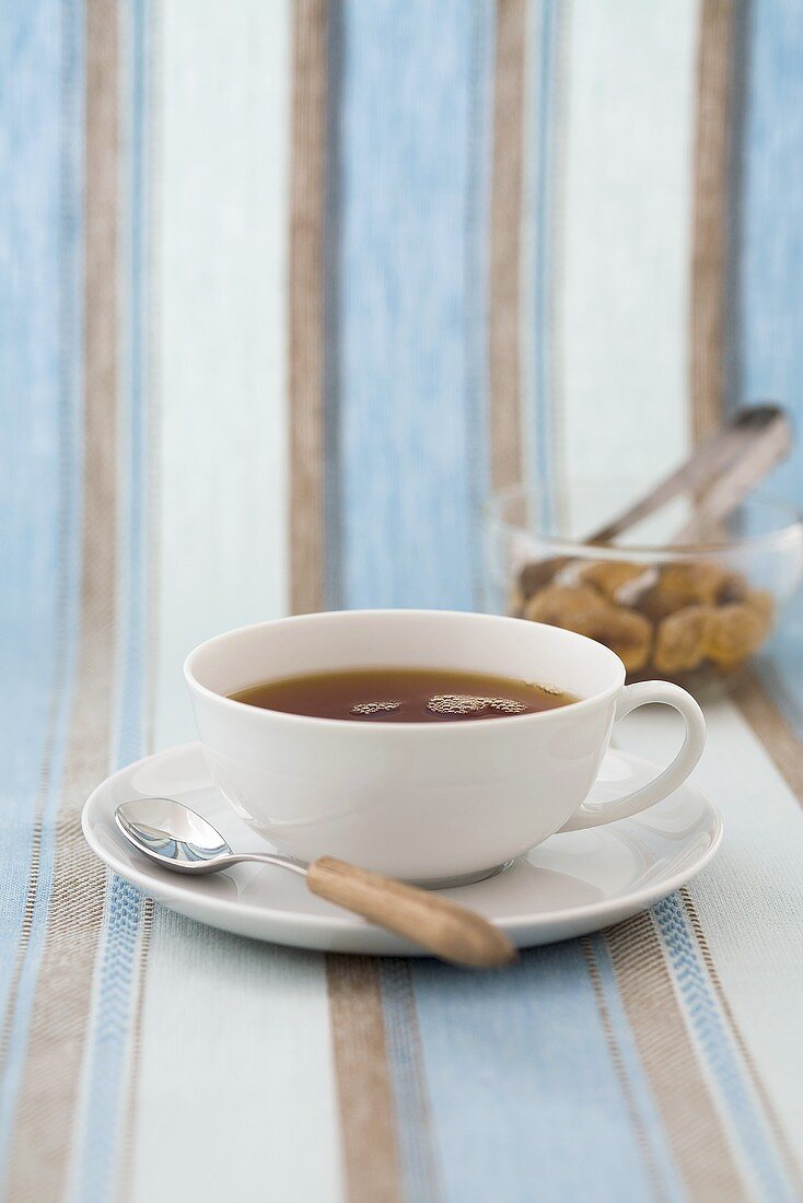 A cup of black tea, glass bowl of sugar crystals behind