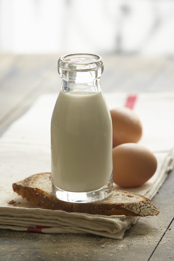 Flasche Milch, Brotscheibe und Eier auf Geschirrtuch