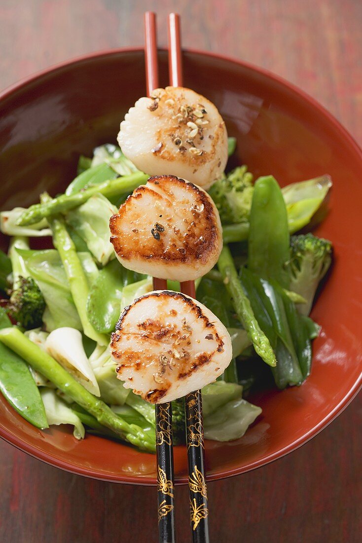 Fried scallops on chopsticks over vegetables (Asia)