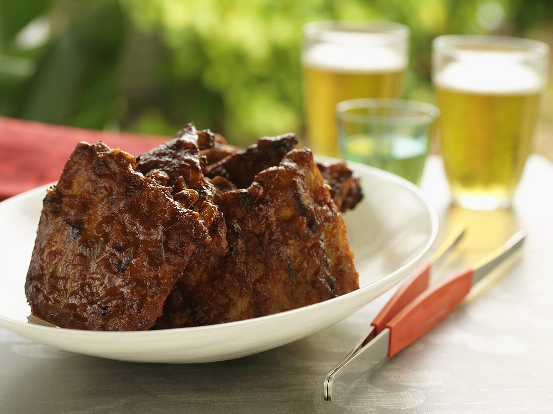 Gegrillte Spareribs auf Tisch im Freien, Bier im Hintergrund