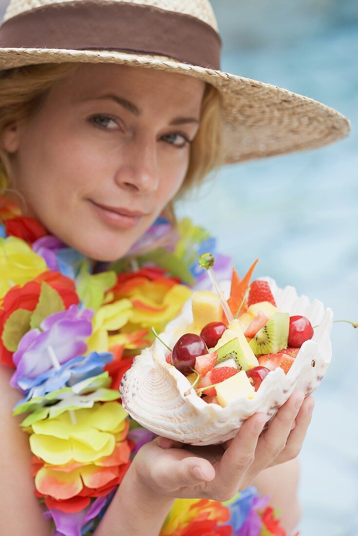 Woman holding shell full of fresh fruit by sea