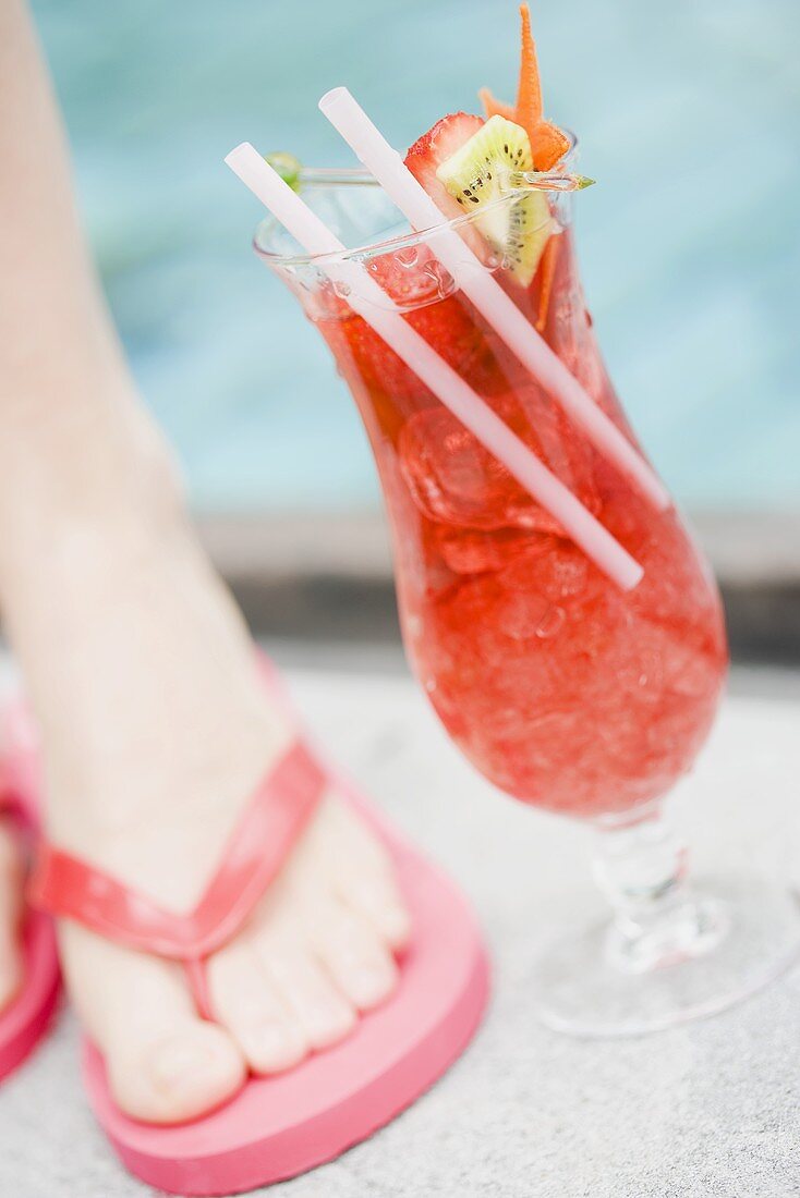Fruity strawberry drink by swimming pool beside someone's foot
