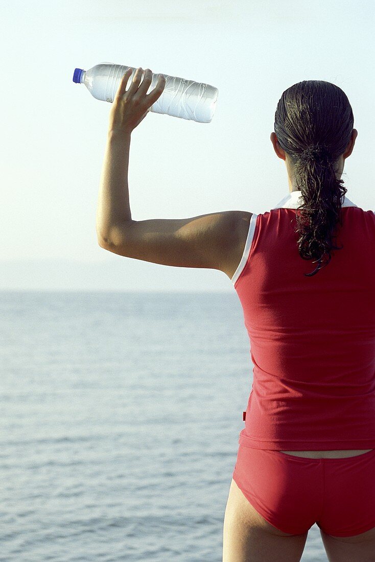 Junge Frau am Strand mit Wasserflasche in der Hand