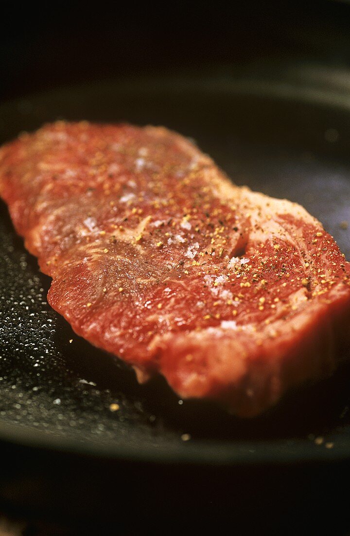 Raw steak seasoned with salt and pepper in a frying pan