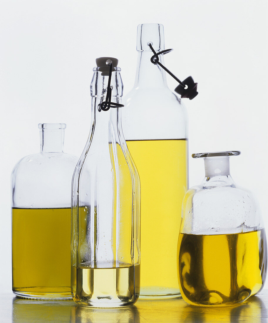 Various types of edible oils in bottles against white background