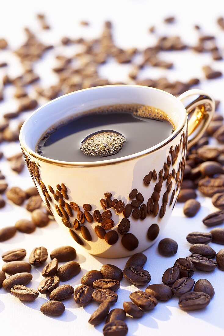 Eine goldene Tasse Kaffee von Kaffeebohnen umgeben